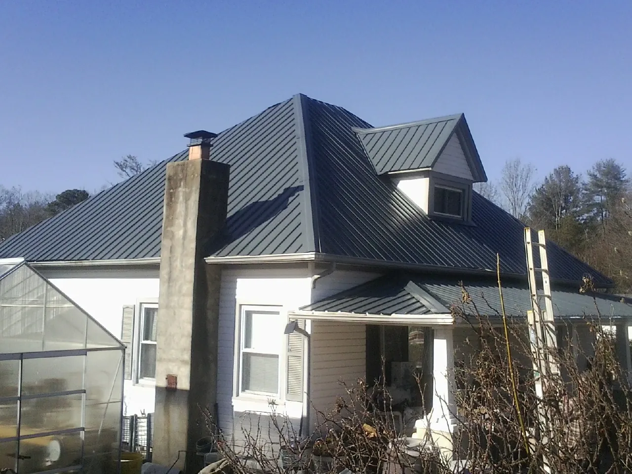 Dark blue standing seam metal roof on a white farmhouse with dormer — Slate & Tile Roof Repair by Roofing Brothers in Churdan