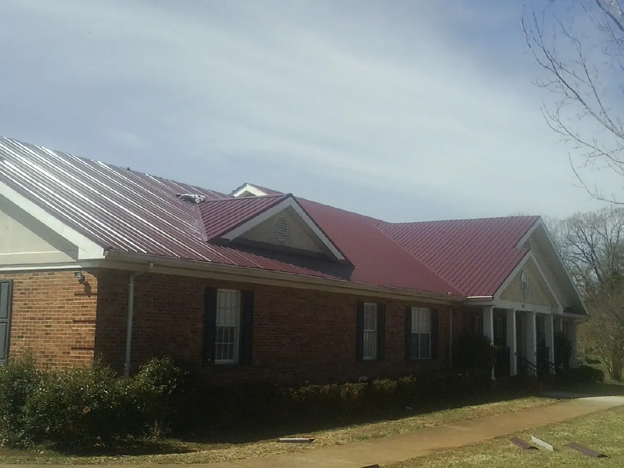 Red metal roof with gabled entries on a long brick building, from a Hail Damage Roof Repair job in Churdan