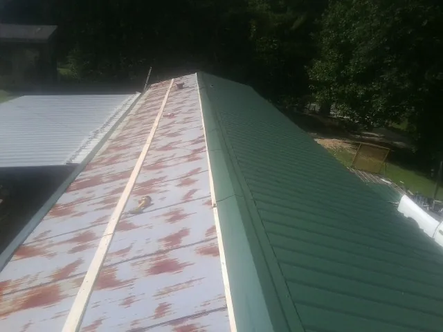 Old rusted panels beside newly installed green metal roofing — Wind Damage Roof Repair by Roofing Brothers in Churdan