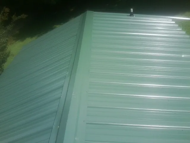 New green metal panels meeting at the ridge of a roof — Flat Roof Repair work by our crew in Churdan