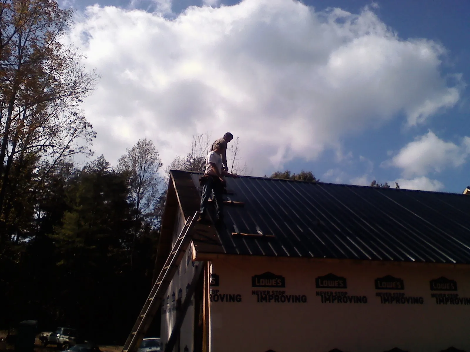 Roofer fastening dark metal panels high against a cloudy sky, from a Roof Inspection job in Churdan