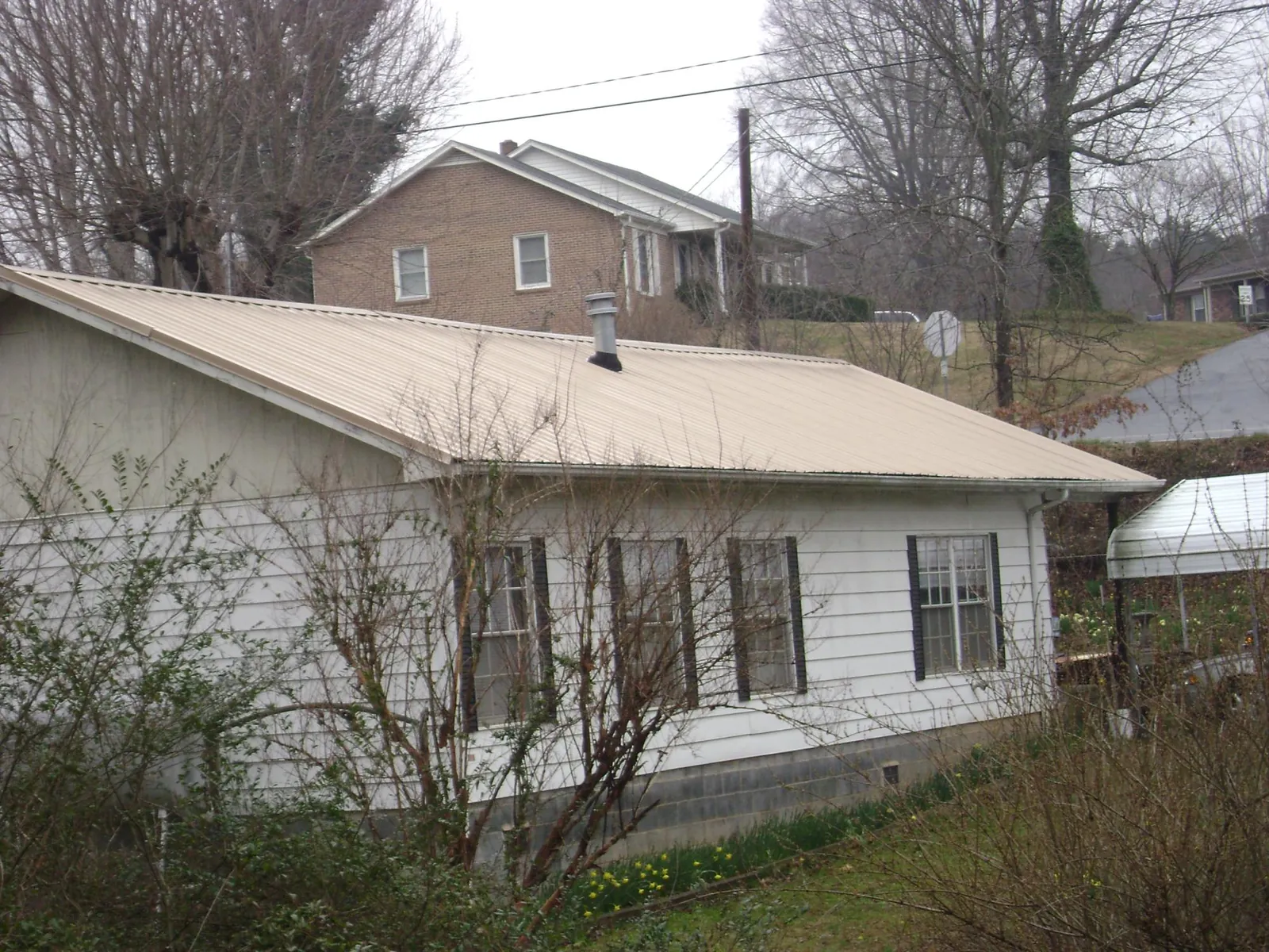 Tan metal roof on a white sided house set into a hillside — Commercial Roofing by Roofing Brothers in Churdan