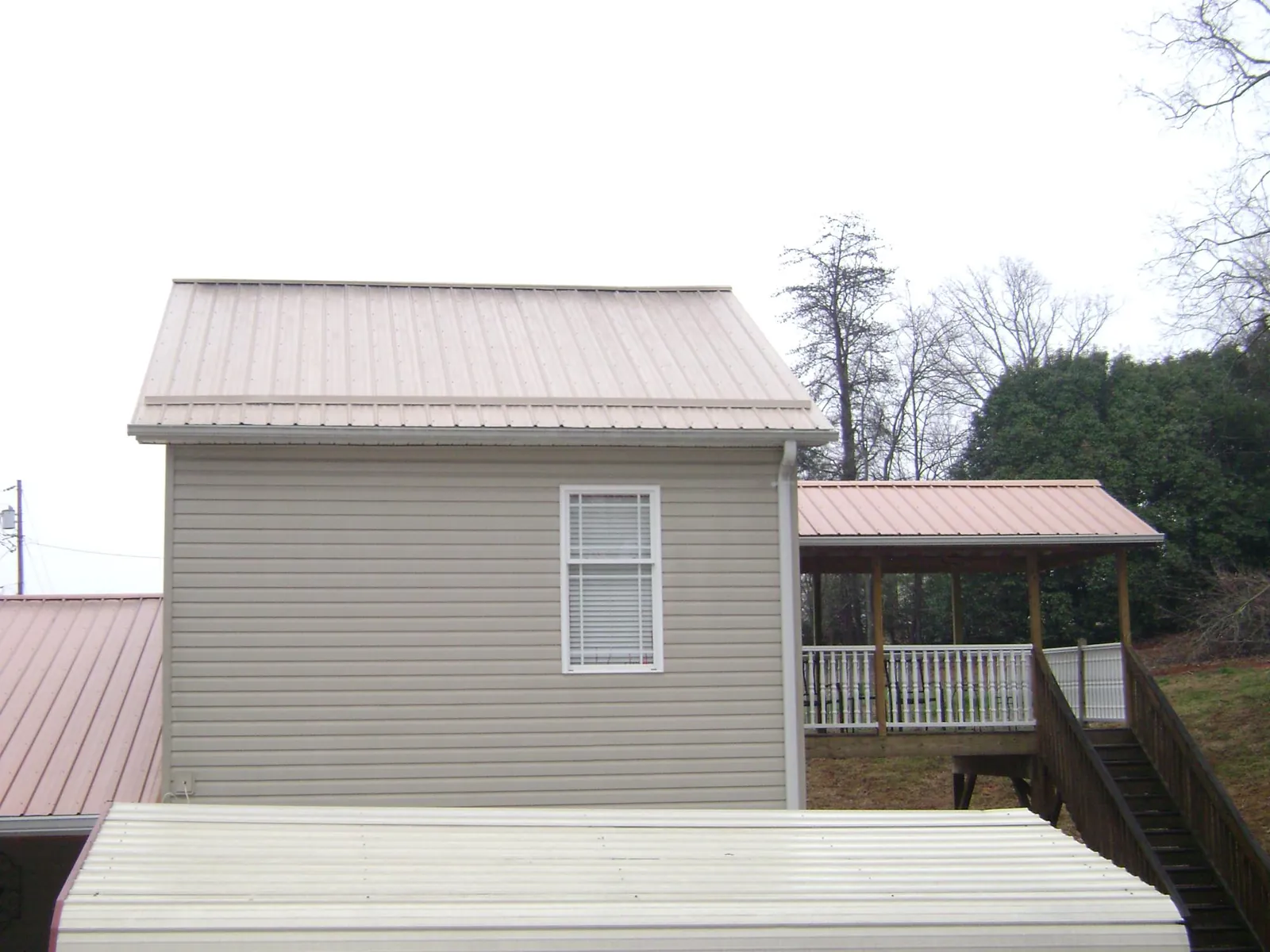 Tan metal roofs on a two story addition and attached porch, from a Roof Replacement job in Churdan